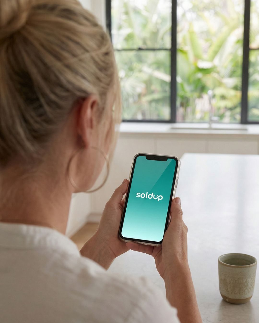 Woman using SoldUp app at kitchen bench